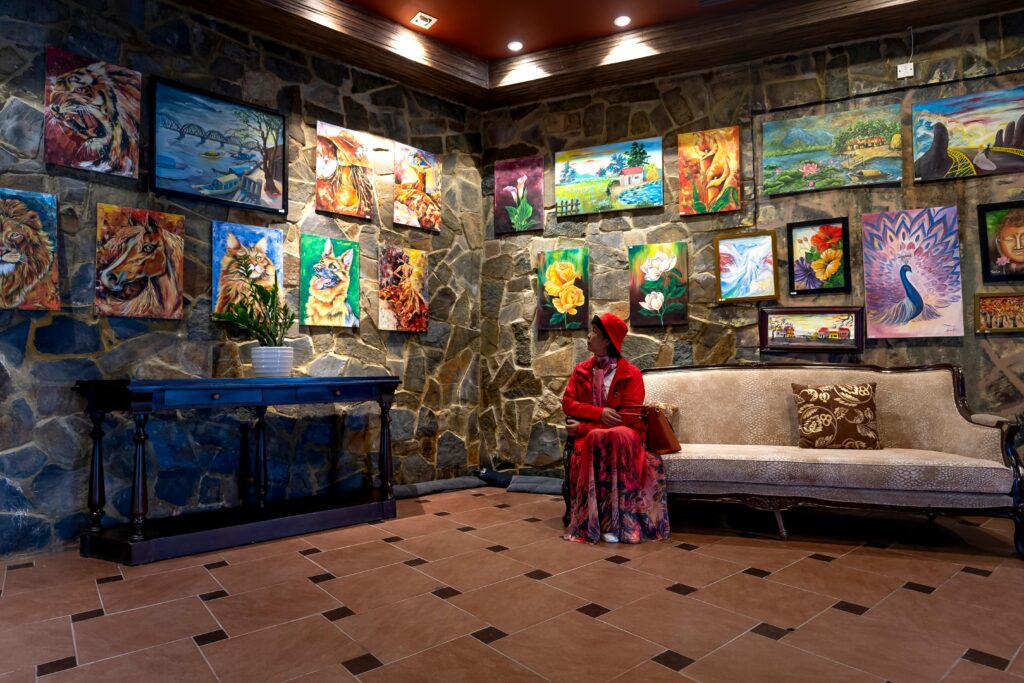 A woman in red sitting in a luxurious art gallery lobby surrounded by colorful paintings.